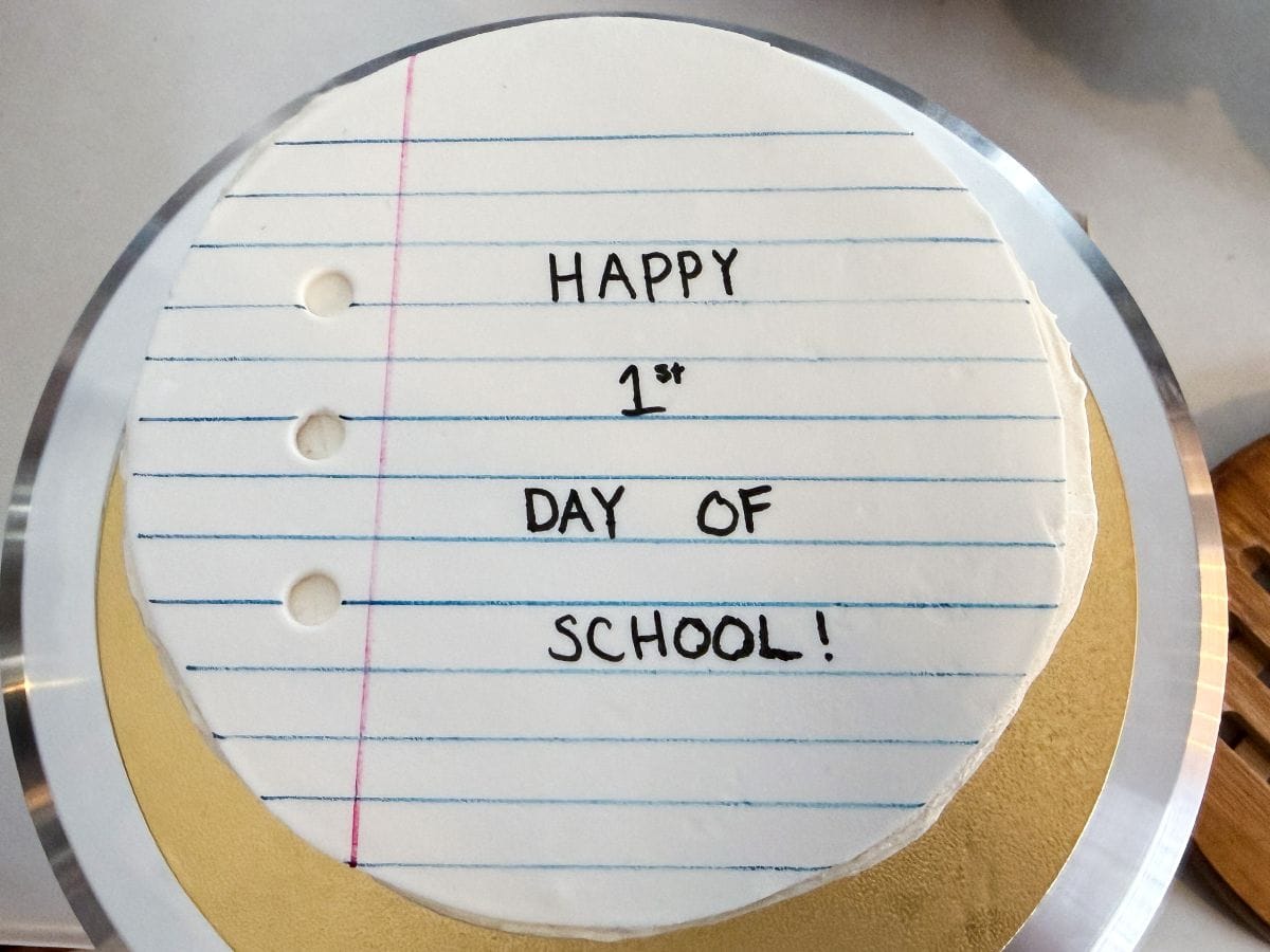 a round rolled fondant topper that looks like a piece of loose leaf paper on top of a round layer cake