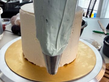 a piping bag fitted with a decorative metal tip in front of a white layer cake
