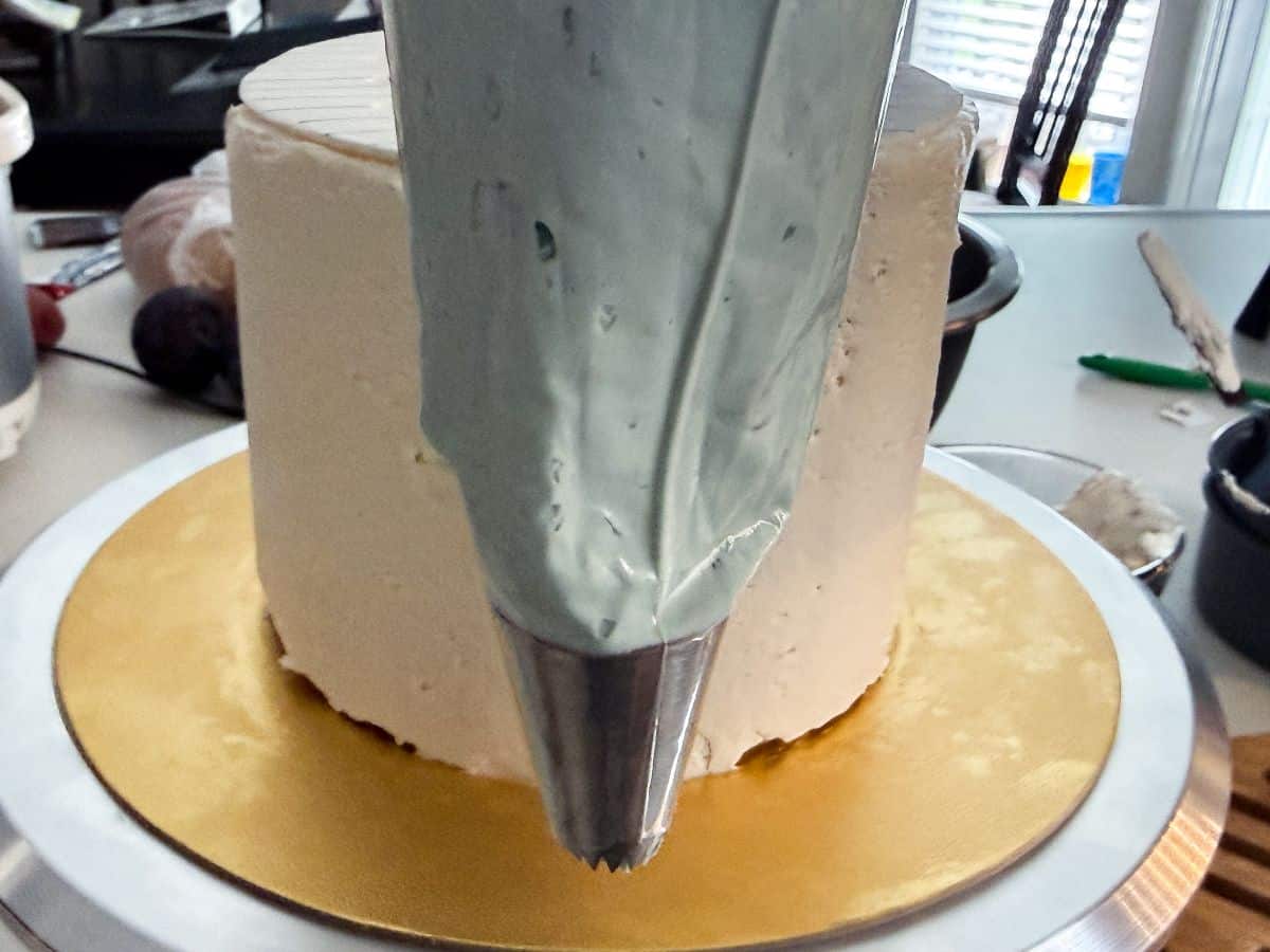 a piping bag fitted with a decorative metal tip in front of a white layer cake