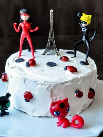 Miraculous Birthday Cake topped with an Eiffel Tower. Cat Noir, Ladybug, Tikka and Plagg figurines and fondant ladybugs