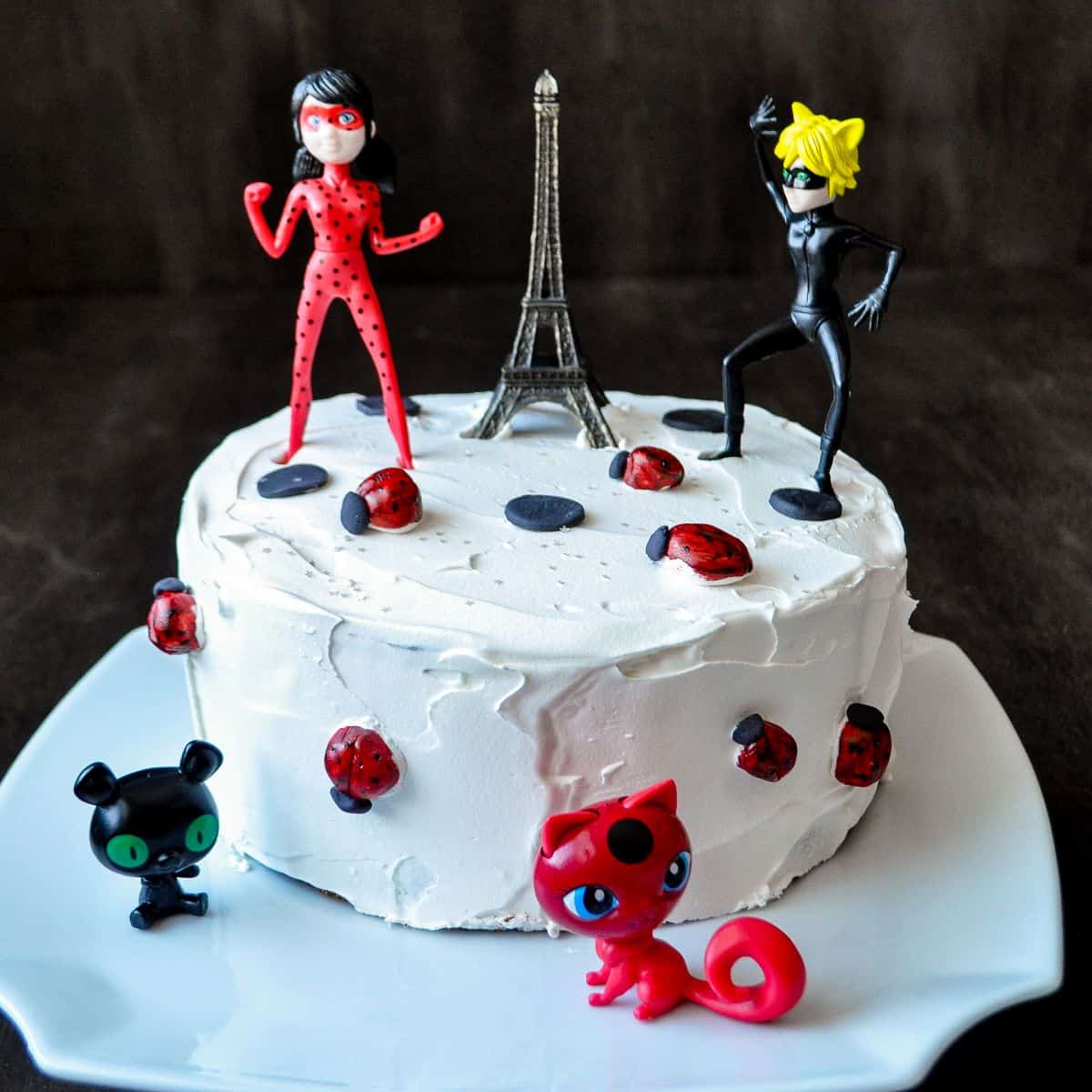 Miraculous Birthday Cake topped with an Eiffel Tower. Cat Noir, Ladybug, Tikka and Plagg figurines and fondant ladybugs
