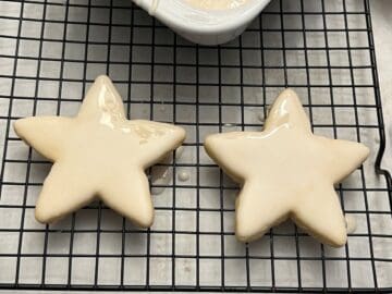 two star cookies on a cooling rack that have just been dipped in cookie icing